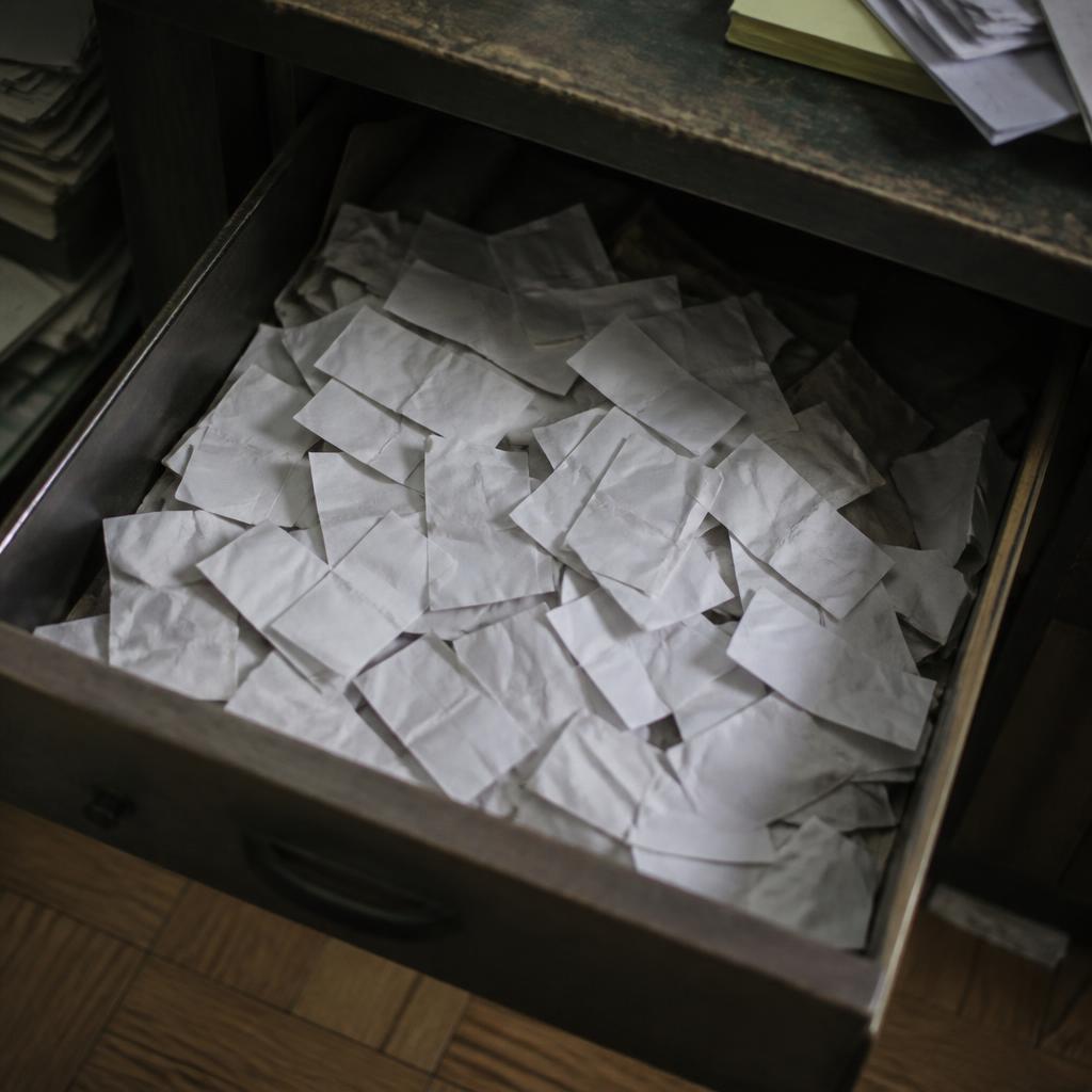 A cluttered desk drawer full of creased, forgotten paper business cards